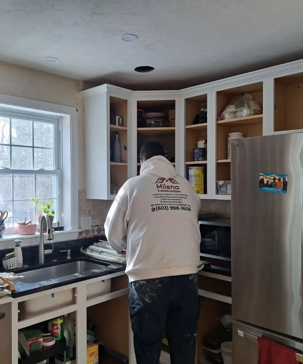 A Milena Construction team member in a branded hoodie painting cabinets on the job in Southern NH