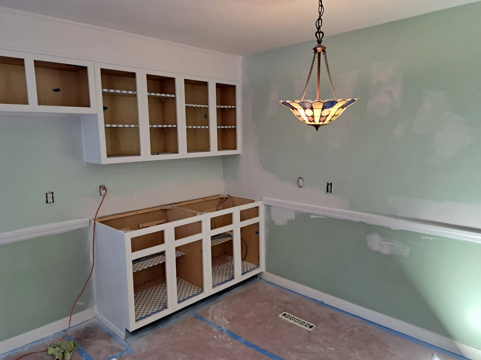 Kitchen cabinets being repainted white against a sage accent wall