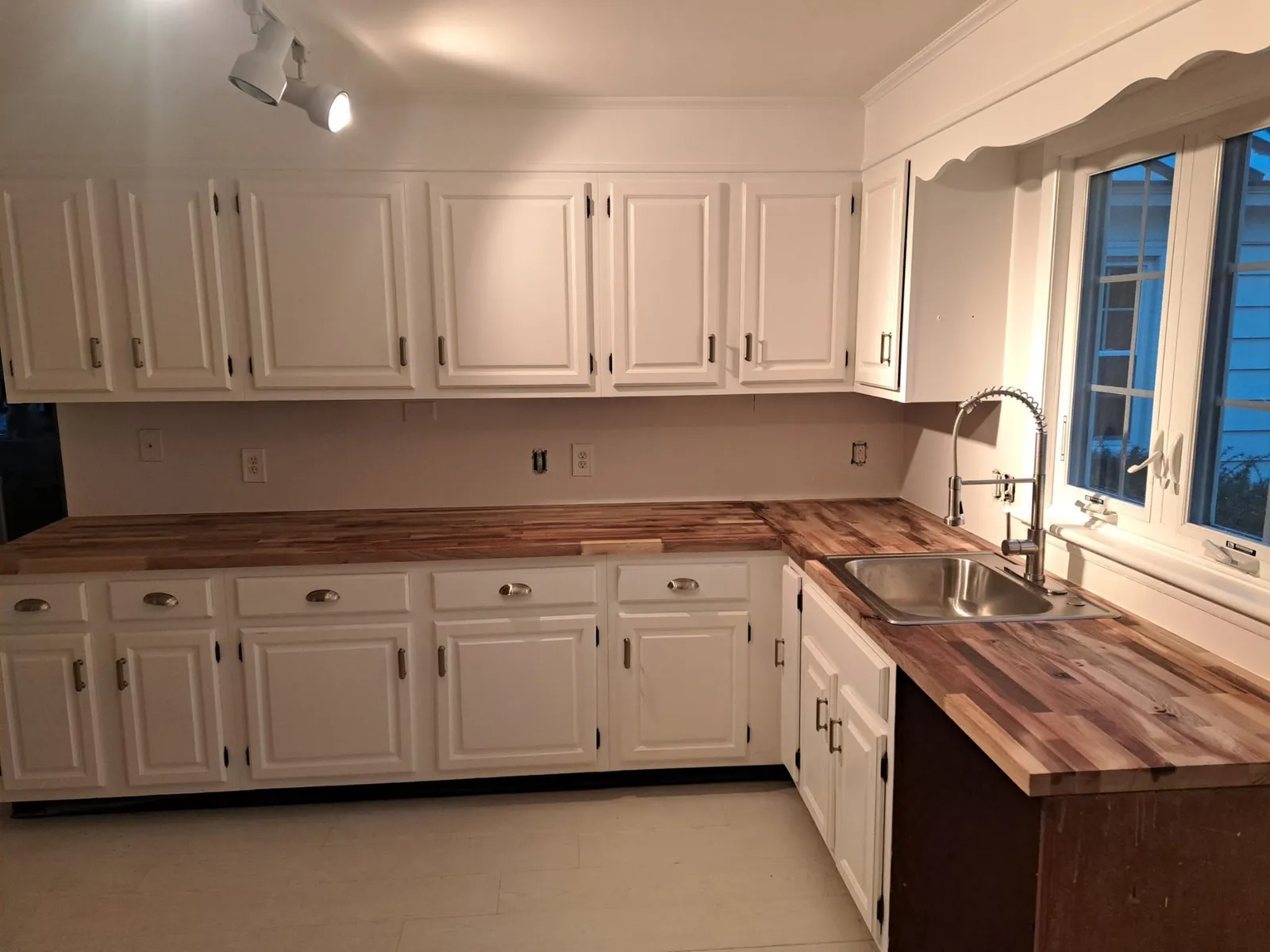 Completed white kitchen with wood counters and a corner sink