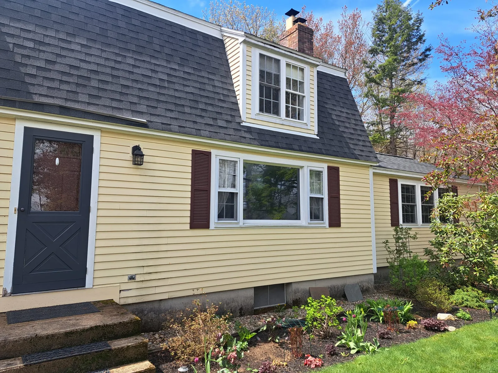 Yellow cape-style home with black shutters after an exterior repaint