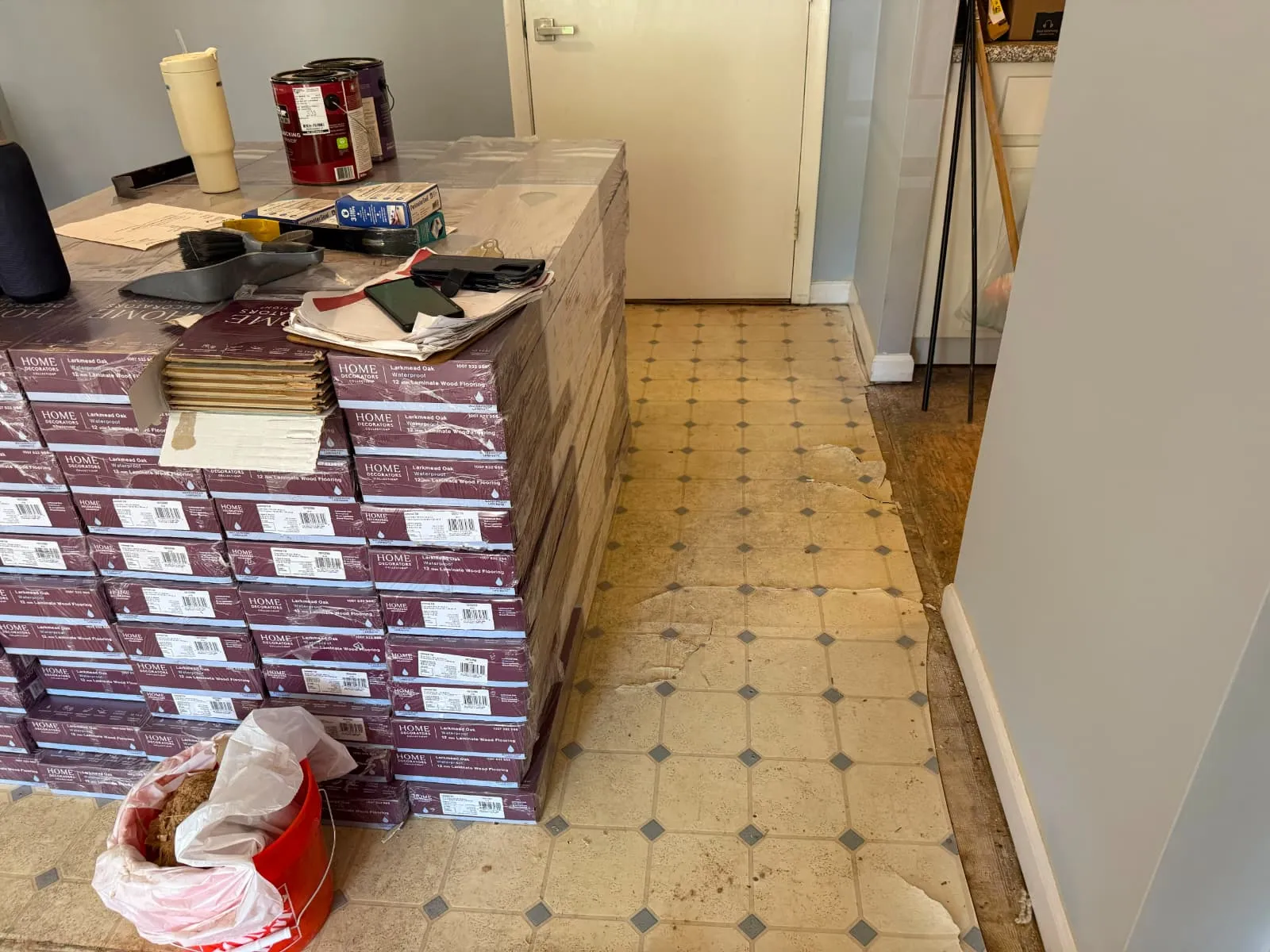 Boxes of new flooring staged over black-and-white tile